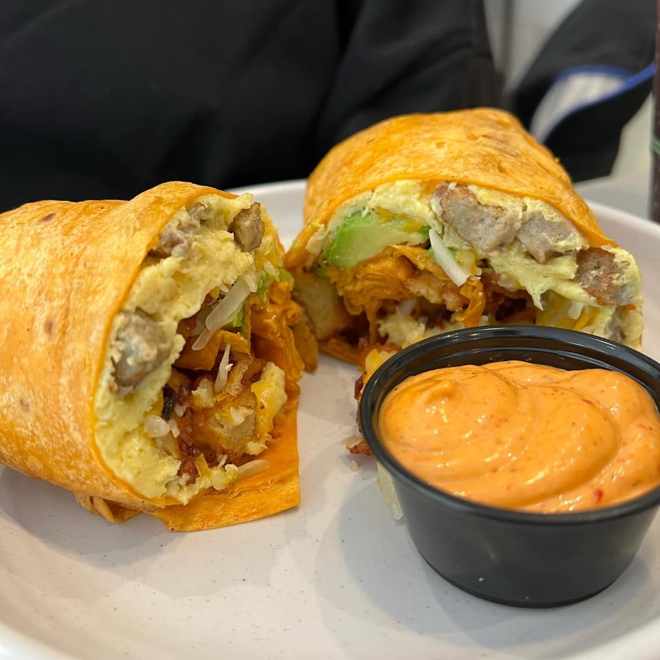 A breakfast burrito from Joe Donut Mt Prospect, cut in half, with a side of orange dipping sauce.