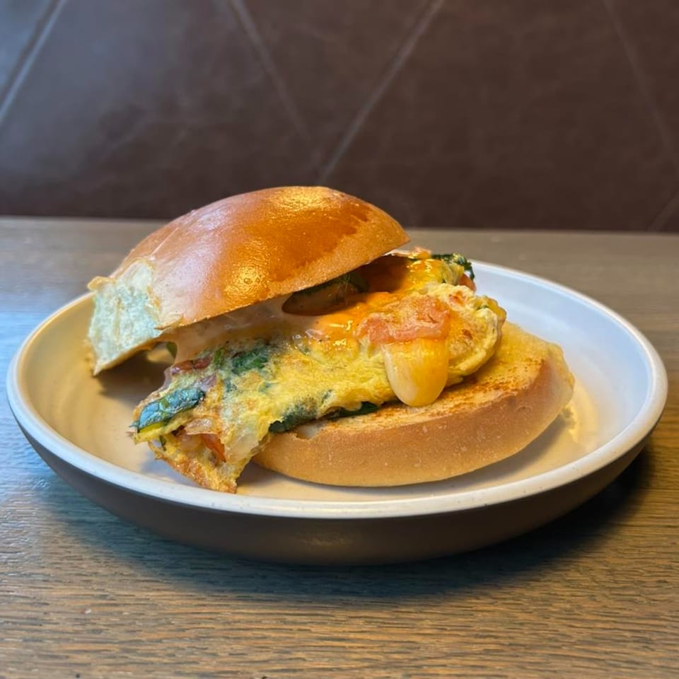 A Joe Donut breakfast sandwich with egg, cheese, and greens on a brioche bun.