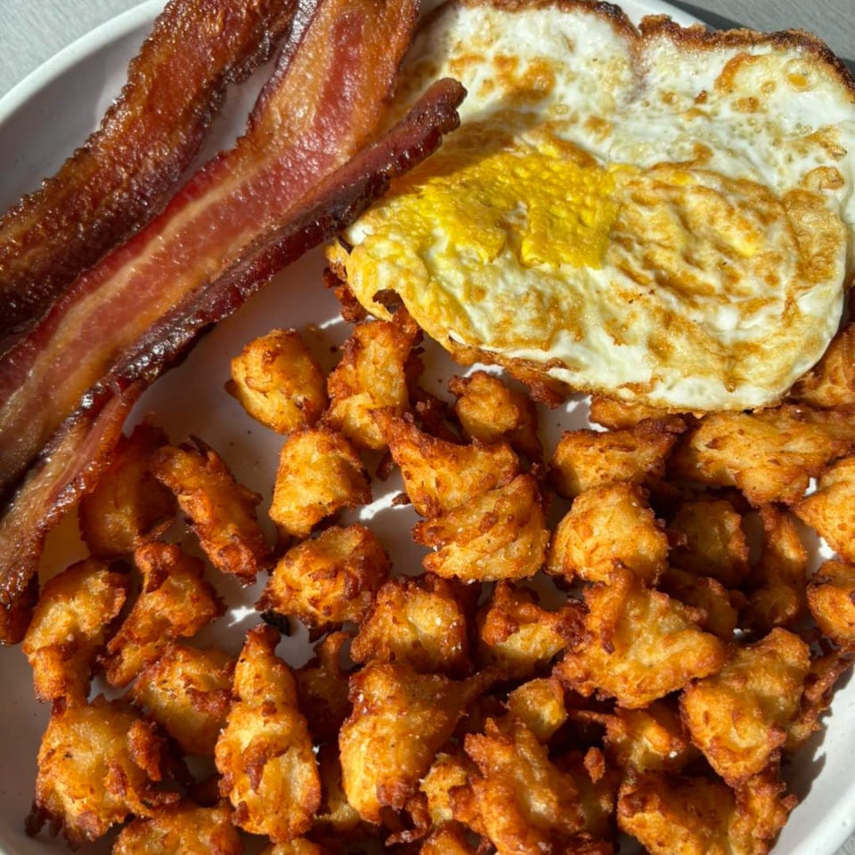 Crispy bacon strips, a fried egg, and golden tater tots on a white plate.