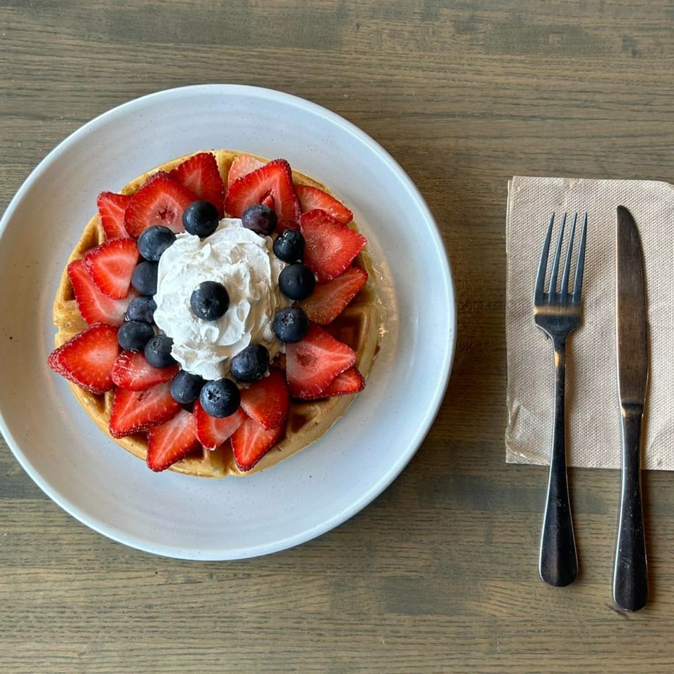 A Joe Donut waffle topped with strawberries, blueberries, and whipped cream on a white plate.
