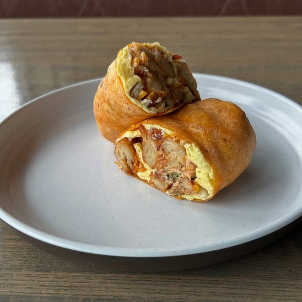 A Joe Donut breakfast burrito, cut in half, revealing eggs, potatoes, and meat on a white plate.