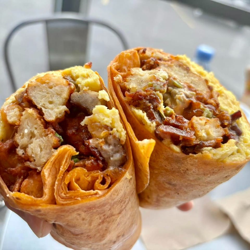 A Joe Donut breakfast burrito, cut in half, revealing eggs, potatoes, and meat inside.