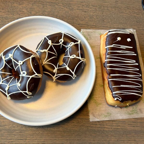 Two chocolate spiderweb donuts on a plate and one chocolate mummy donut on paper at Joe Donut.
