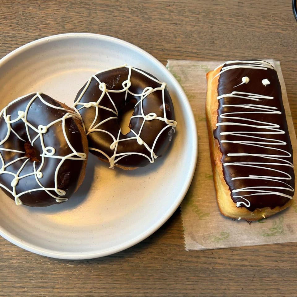 Two chocolate spiderweb donuts on a plate and one chocolate mummy donut on paper at Joe Donut.